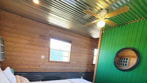 Une pièce avec un lit, un ventilateur de plafond, une fenêtre et un mur vert.