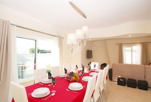 Een eetkamer met een rode tafelkleed, witte stoelen en een kroonluchter.