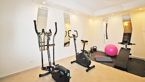 Une salle de sport à domicile équipée de deux vélos d’appartement, d’un appareil elliptique, d’un tapis de course et d’un ballon d’exercice rose.