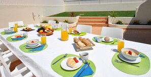 Een buitenontbijtzone met tafels, belegd met fruit, gebak en drankjes.