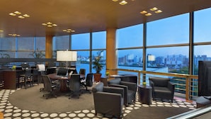 A modern hotel lobby with a large desk area, comfortable seating, and a view of the cityscape through large windows. - Quinto Centenario Hotel (Córdoba)
