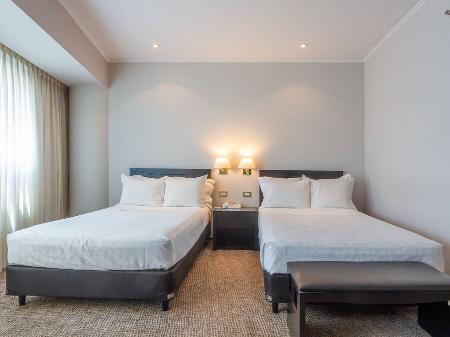 Une chambre d’hôtel avec deux lits, un banc et une table de chevet avec des lampes.