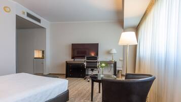 Ein Hotelzimmer mit Bett, Schreibtisch, Stuhl, Lampe und einem großen Fenster mit Vorhängen.