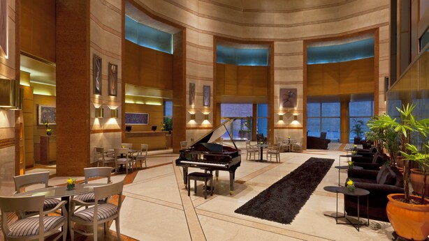 A spacious lobby with a grand piano, seating areas, and a large potted plant. - Quinto Centenario Hotel (Córdoba)