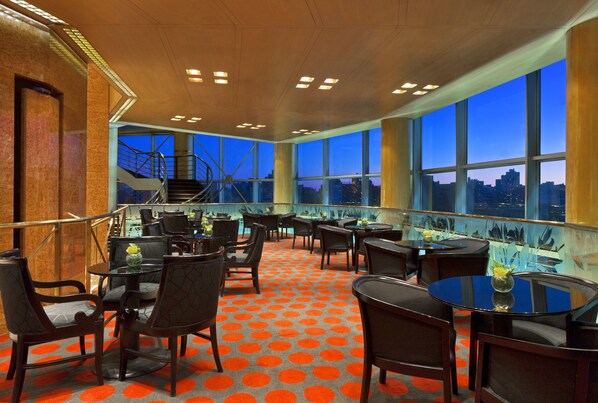A restaurant with a view of the city at dusk, featuring a spiral staircase, round tables, and chairs with orange accents. - Quinto Centenario Hotel (Córdoba)