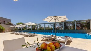 A poolside area with lounge chairs and umbrellas, a table with fruit, and a clear blue pool. - Quinto Centenario Hotel (Córdoba)