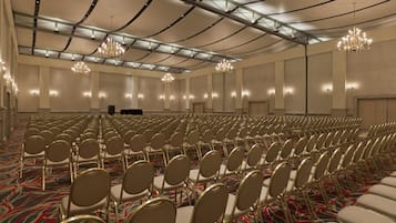 A large conference room with rows of chairs, chandeliers, and a stage.
