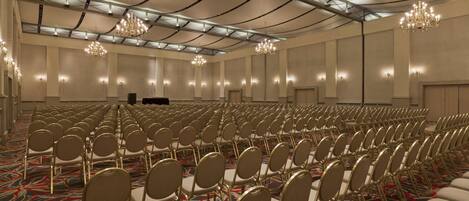 A large conference room with rows of chairs, chandeliers, and a stage.