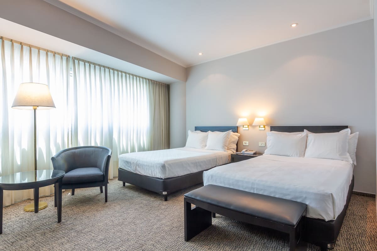 Une chambre d’hôtel avec deux lits, une chaise, une table et un banc.