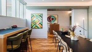Een moderne eetruimte met een lange tafel, stoelen en abstracte muurkunst.