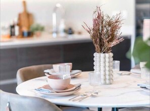 Una mesa de comedor dispuesta con platos, fuentes y cubiertos, y un florero con flores secas.