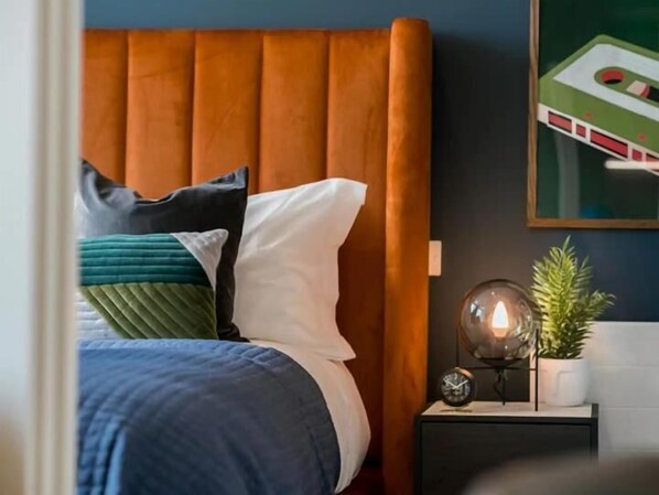 A bedroom with a bed, pillows, a nightstand, a clock, and a plant.
