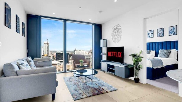 A modern living room with a sofa, a coffee table, a TV, and a view of the city through large windows.