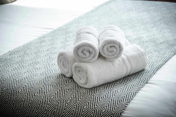 A neatly folded set of white towels stacked on a patterned pillow on a bed.