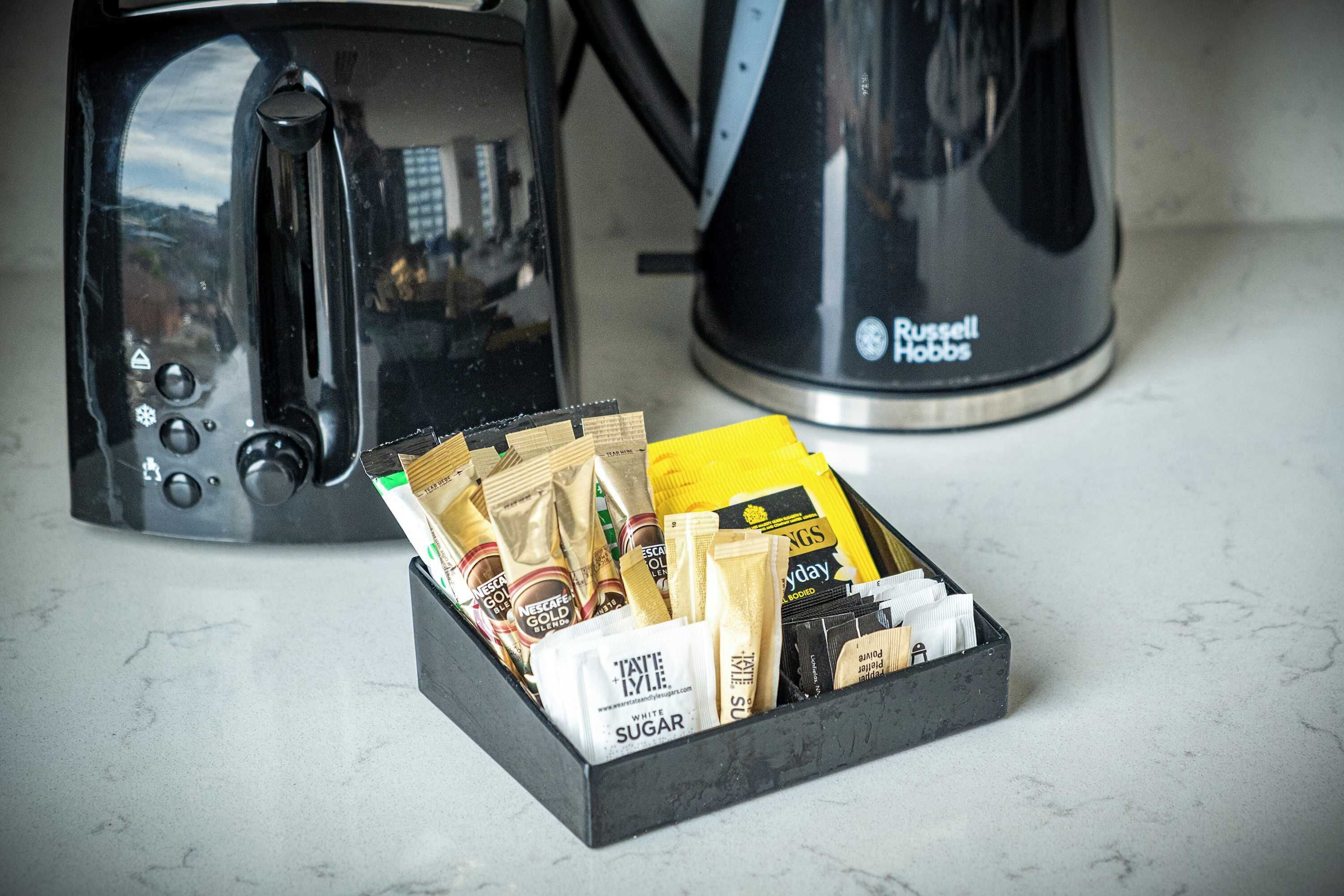 En köksbänk med en kaffebryggare, en vattenkokare och en förpackning kaffekapslar.