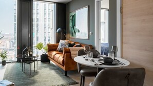 A modern living room with a sofa, a dining table, and a large window offering a city view. - The Mercian 1 XVIII- 1BDR |STUNNING CITY SKYLINE VIEWS! 24-Hour GYM | CINEMA room (West Midlands)