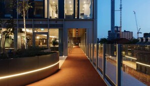 A modern building with a glass facade, a curved walkway, and a view of the city skyline. - Your Perfect Stay l The Mercian Bldg., 218 Broad Street, Birmingham B15 1AY (West Midlands)