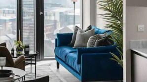 Ein modernes Wohnzimmer mit einem blauen Sofa, einem Esstisch mit Stühlen und einem großen Fenster mit Blick auf die Stadt.