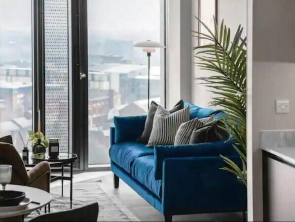 A modern living room with a blue sofa, a dining table with chairs, and a large window with a city view.
