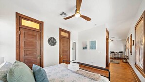 Un dormitorio con cama, puertas de madera, ventilador de techo, un reloj y un pasillo con zona de comedor.