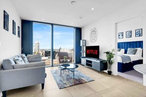 A modern living room with a sofa, a coffee table, a TV, and a view of the city through large windows. - Striking City View| 24 Hrs Gym| Free Netflix (West Midlands)