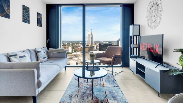 Una sala de estar moderna con un sofá gris, una mesa de centro, un televisor y un ventanal con vistas a la ciudad.