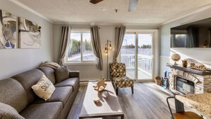A living room with a sofa, armchair, coffee table, fireplace, and large windows.