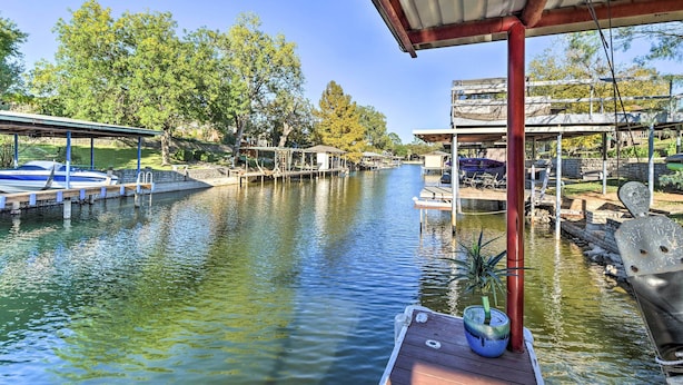 A canal with boats docked on the left, a covered area with a red pole, and a potted plant on the right. - Granbury Home w/ Lake Granbury Access + Dock! (Granbury)