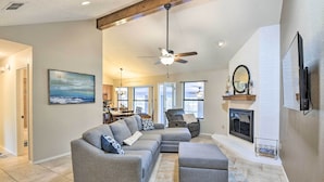 A spacious living room with a gray sectional sofa, a gray ottoman, and a ceiling fan. There is a fireplace with a mirror above it and a dining area in the background. - Granbury Home w/ Lake Granbury Access + Dock! (Granbury)