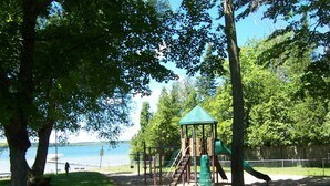 A playground with a climbing structure and slides, surrounded by trees and a body of water.