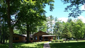 A lodge with a covered porch and a pathway leading to it, surrounded by trees and a well-maintained lawn.