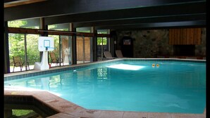 An indoor swimming pool with clear blue water, a basketball hoop, and a stone wall.