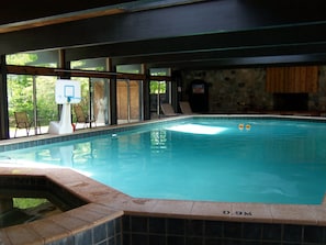 An indoor swimming pool with clear blue water, a basketball hoop, and a stone wall.