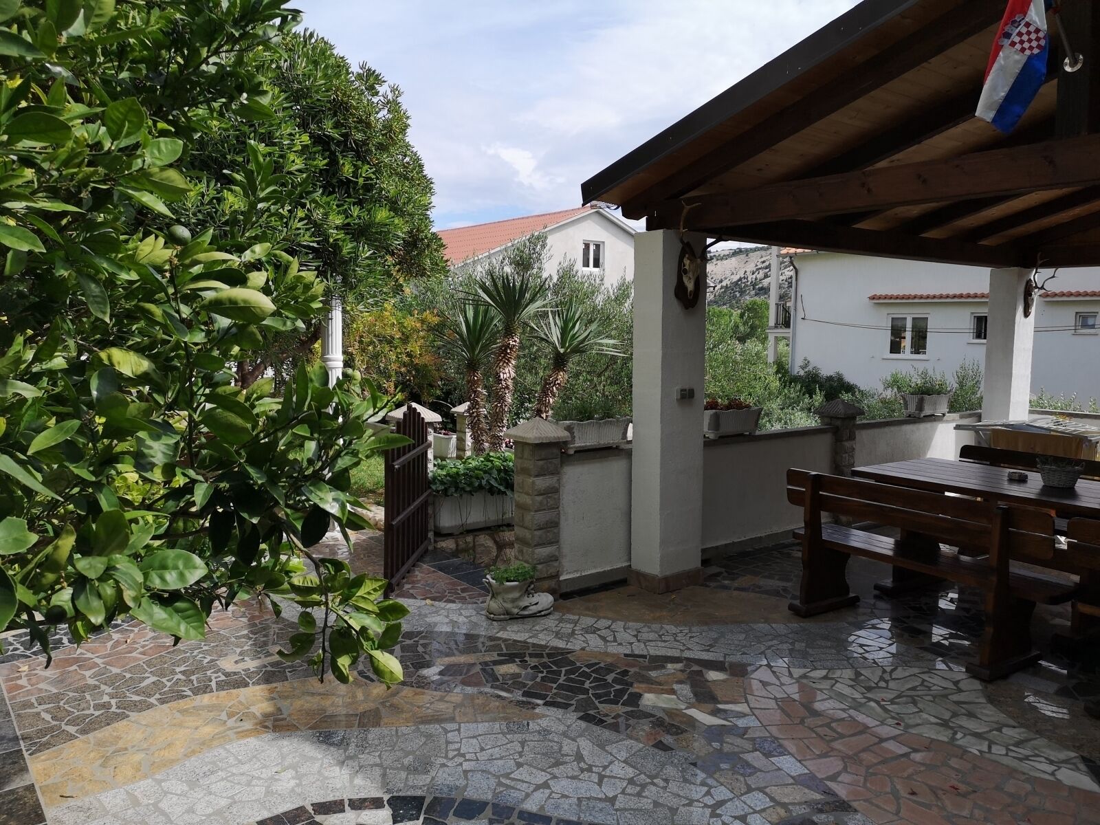 A patio area with a mosaic floor, a wooden table, and a stone wall.