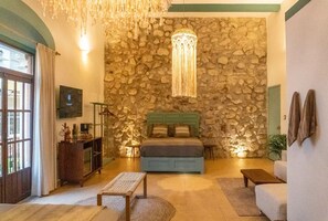 Une chambre avec un mur en pierre, un lit, un lustre et un téléviseur.