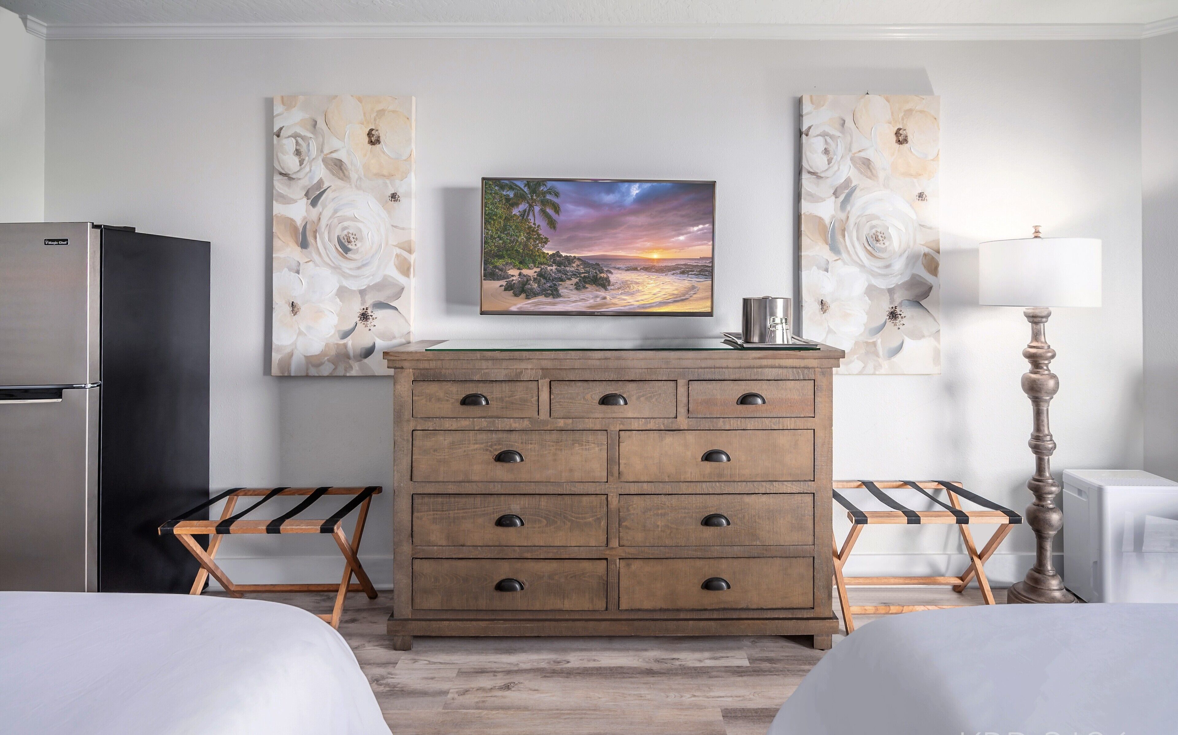 Una habitación de hotel con un aparador de madera, dos camas, un televisor y obras de arte en las paredes.