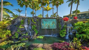 A tropical garden with a sign reading "Kauai Beach Resort," featuring waterfalls, lush greenery, and palm trees. - Oceanfront Resort, 2 QUEEN beds, water views, walk-out access to pools/ocean (Lihue)