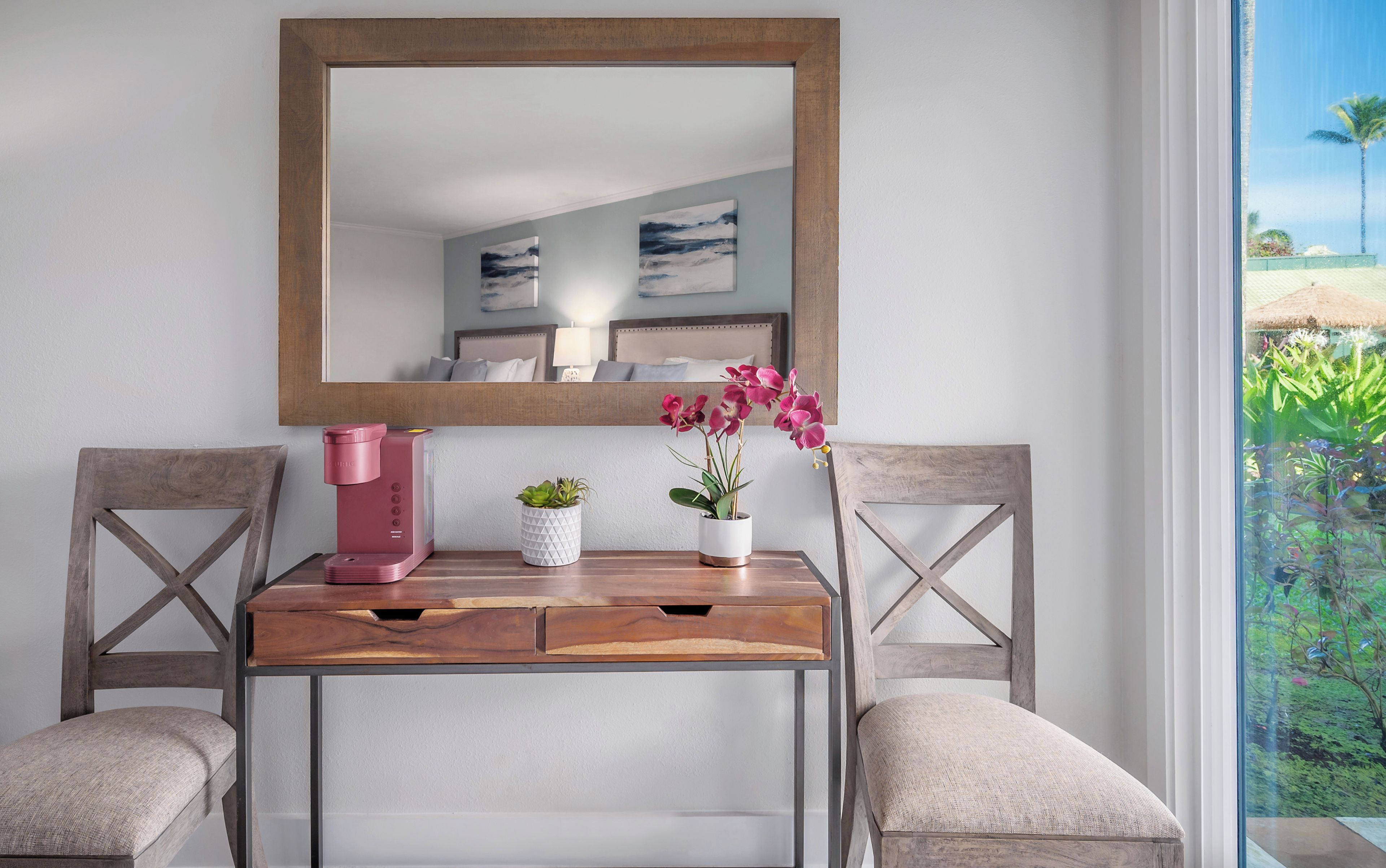 Une chambre moderne avec une console en bois, deux chaises, un grand miroir et une vue sur un jardin, visible à travers une grande fenêtre.