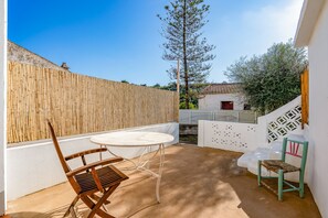 Une terrasse avec une table et des chaises, une clôture en bambou et un mur blanc orné d’un motif géométrique.