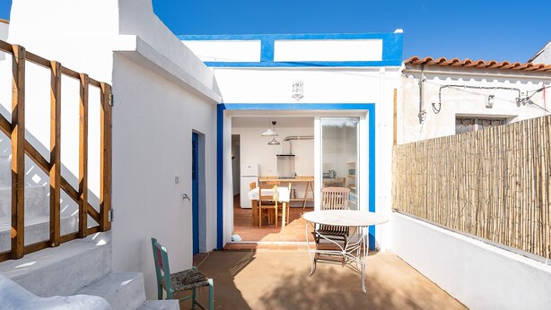A white building with blue trim, a wooden fence, and a patio with a table and chairs. - Quiet and bright village house (Silves)