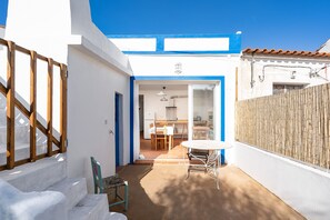 Un bâtiment blanc avec des bordures bleues, une clôture en bois et une terrasse avec une table et des chaises.