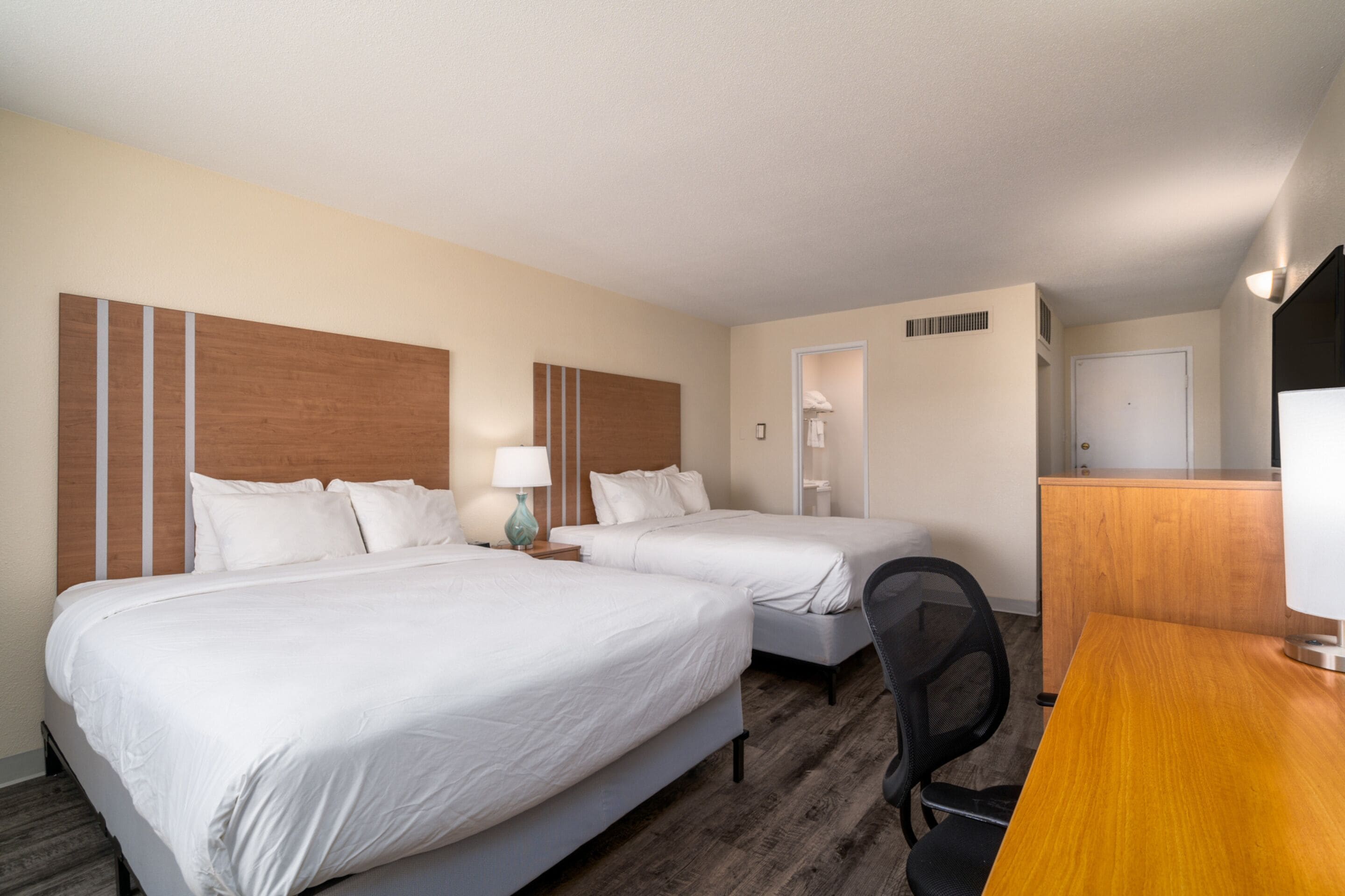 A hotel room with two beds, a desk, and a chair.