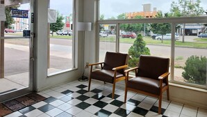 A room with two brown leather chairs, a checkered floor, and large windows offering a view of a parking lot and buildings. - Nevada Flats Hotel (Colorado Springs)