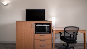 A compact office space with a wooden desk, a black office chair, a microwave, and a television on a cabinet. - Nevada Flats Hotel (Colorado Springs)