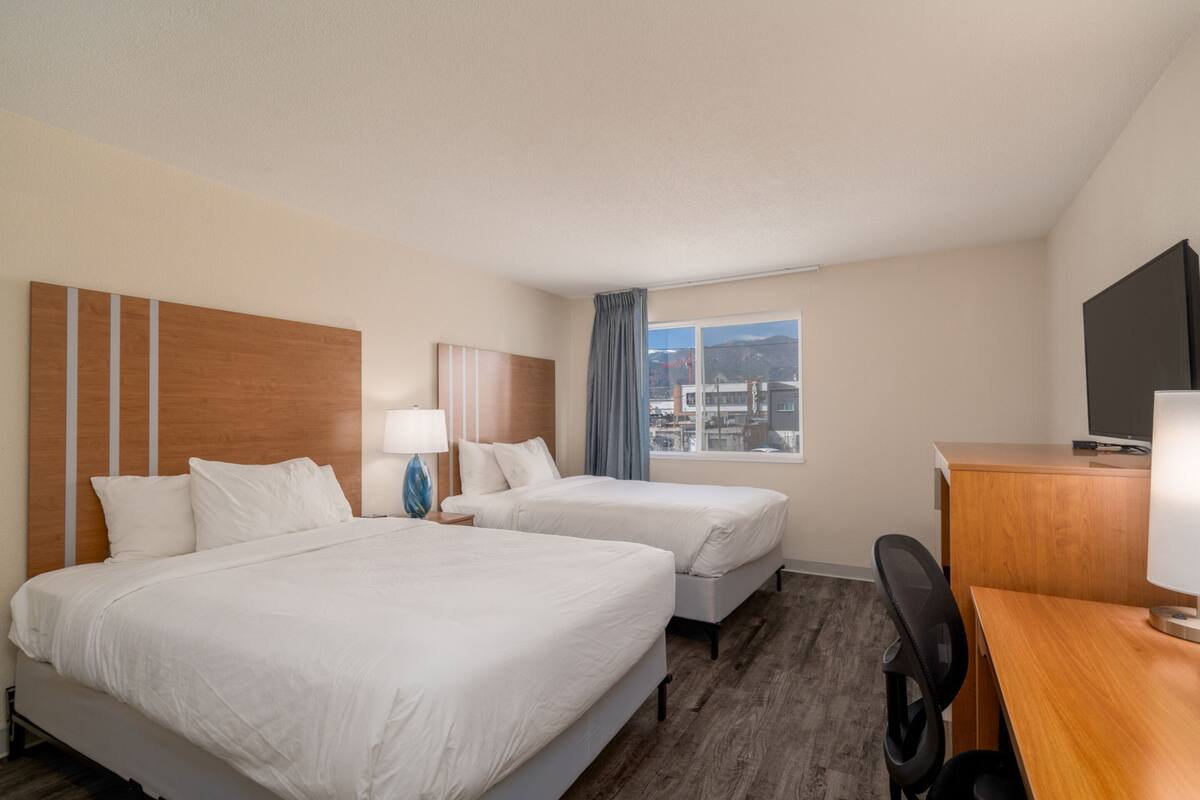 Une chambre d’hôtel avec deux lits, un bureau, une chaise, une télévision et une fenêtre donnant sur la ville.
