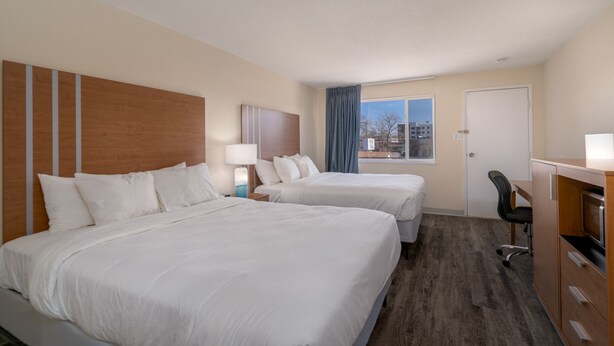 A hotel room with two beds, a desk, a chair, and a window with a view of the city. - Nevada Flats Hotel (Colorado Springs)
