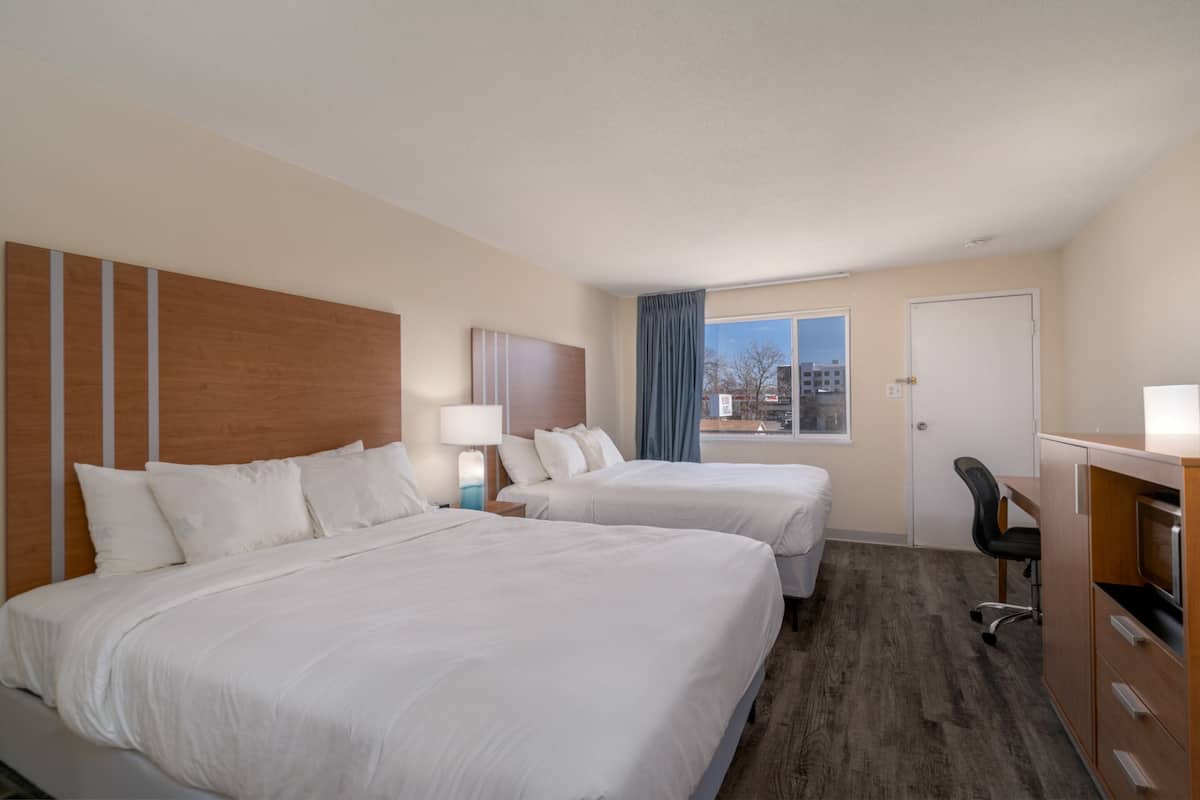 Une chambre d’hôtel avec deux lits, un bureau, une chaise et une fenêtre donnant sur la ville.