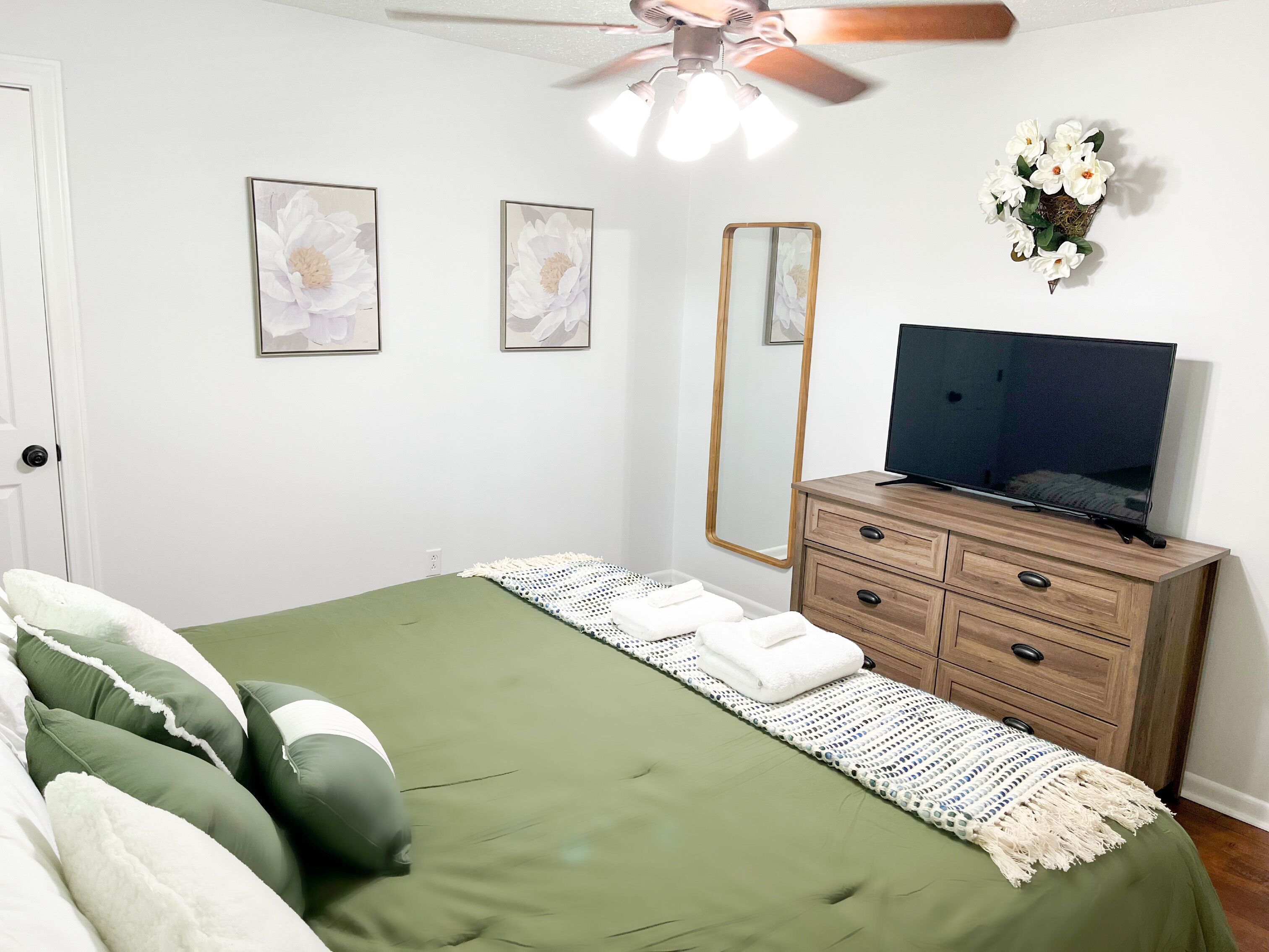 Ein Schlafzimmer mit einem Bett, einem Schminktisch, einem Fernseher und Wandbildern.