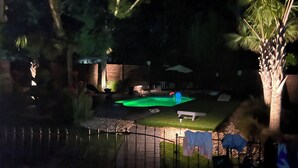Vue nocturne d’une cour arrière avec une petite piscine, un espace patio et une clôture.
