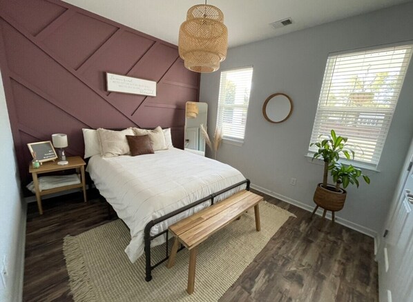 A bedroom with a bed, bedside table, lamp, bench, and a potted plant. - 1/2 Acre Fenced In Private Oasis (Wilmington)